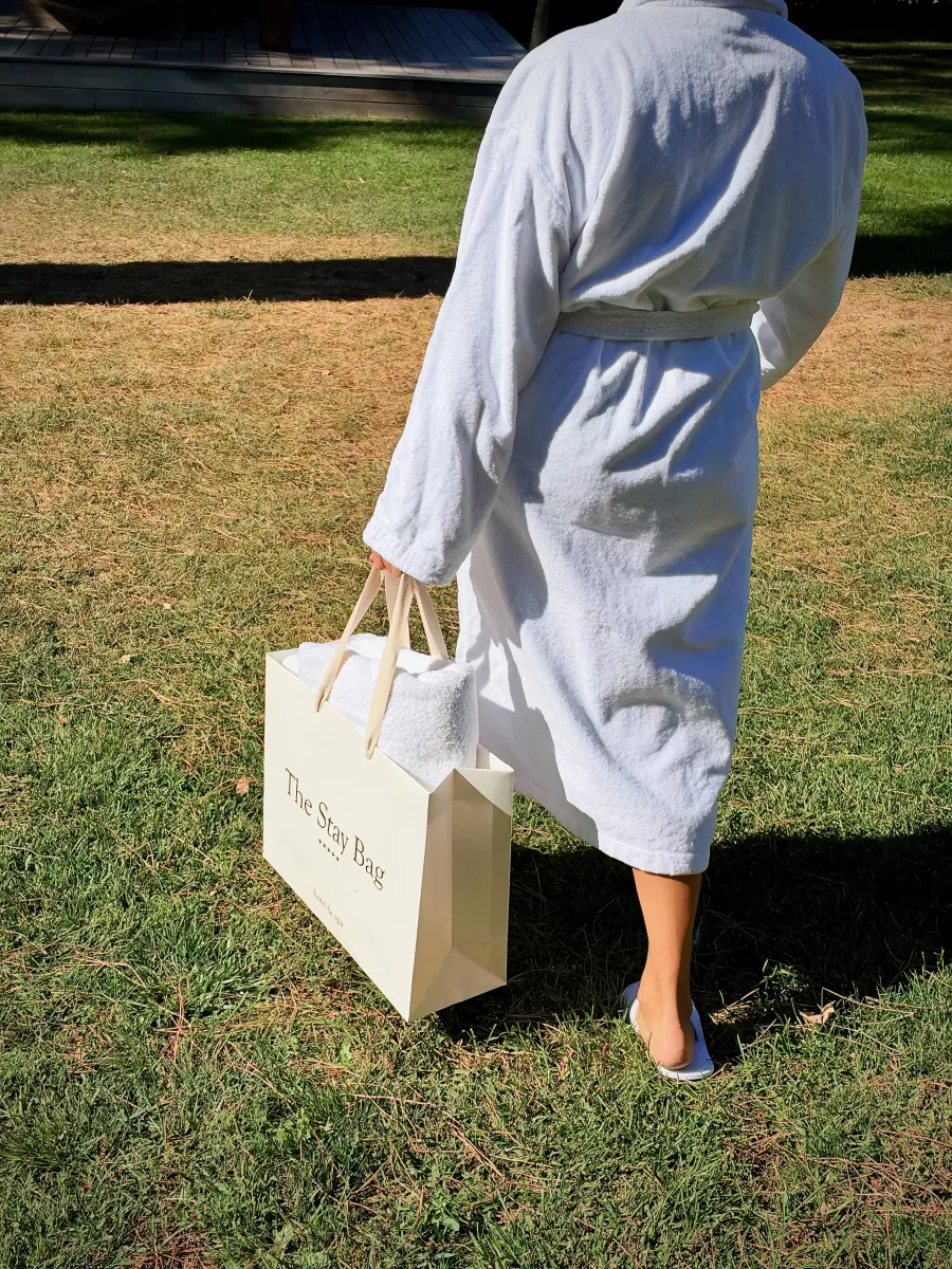 Cliente en peignoir traversant le jardin de l'hôtel avec The Stay Bag à la main
