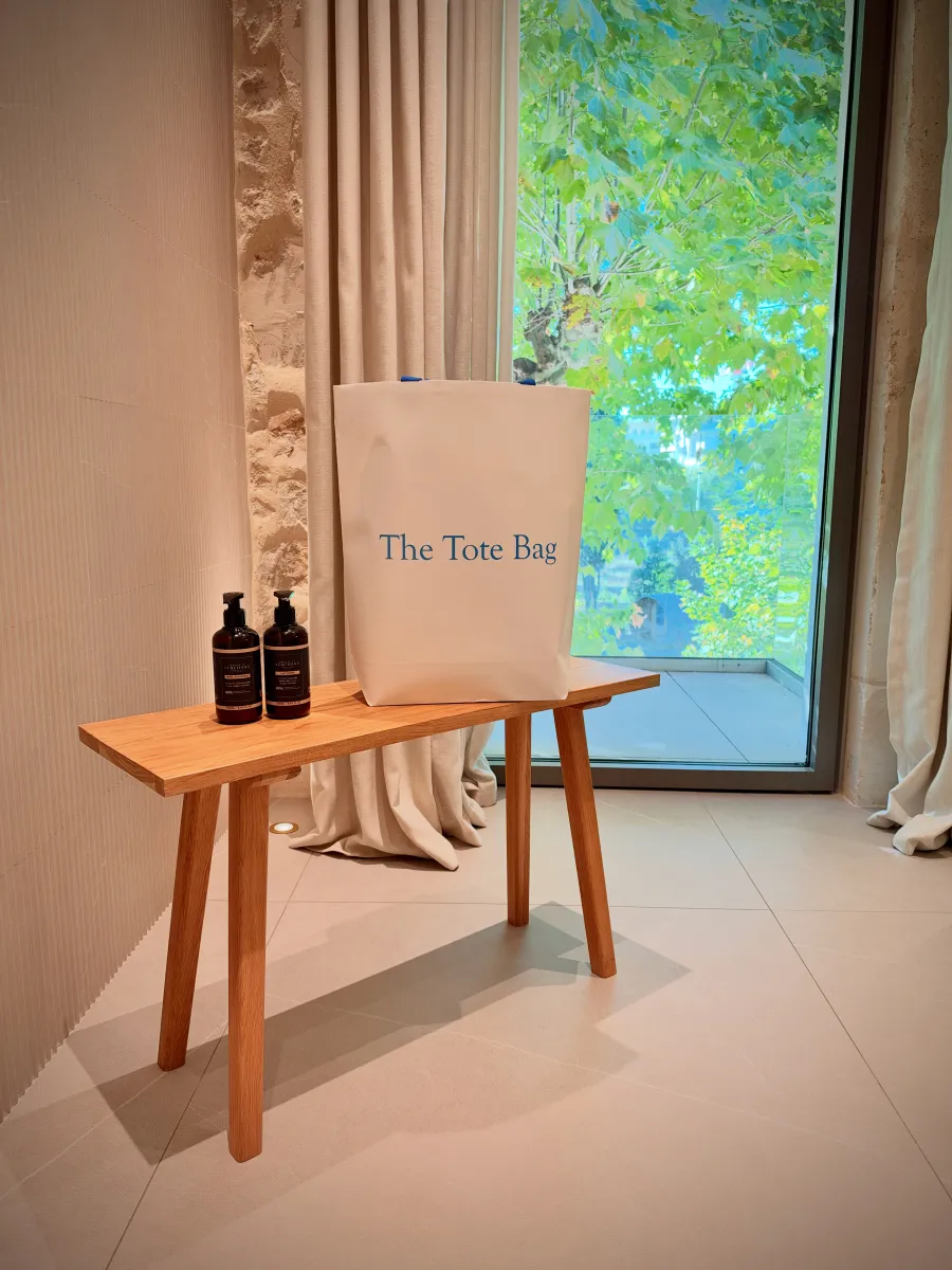 The Tote Bag sur un banc en bois, à côté de flacons de soin
