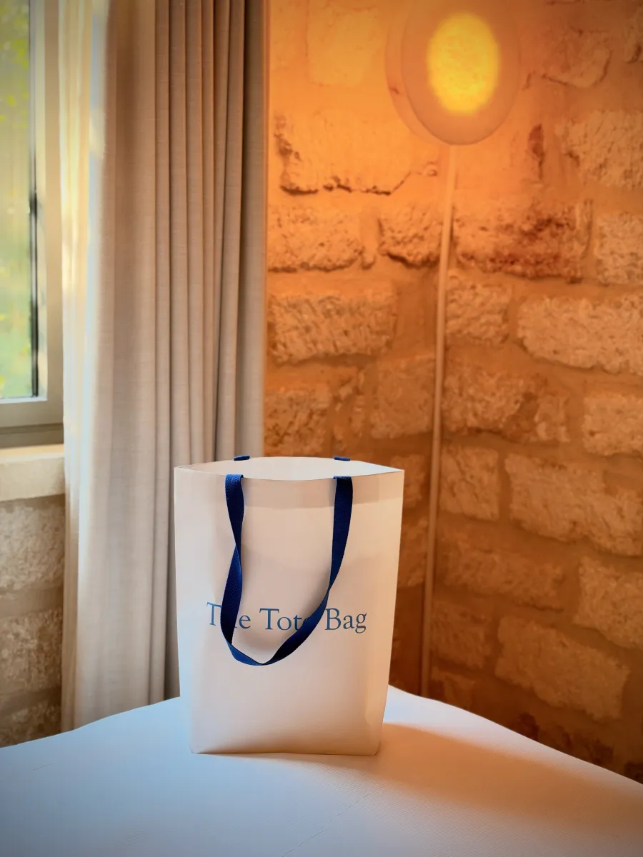 The Tote Bag aux anses bleues posé près d'une fenêtre, lumière chaude