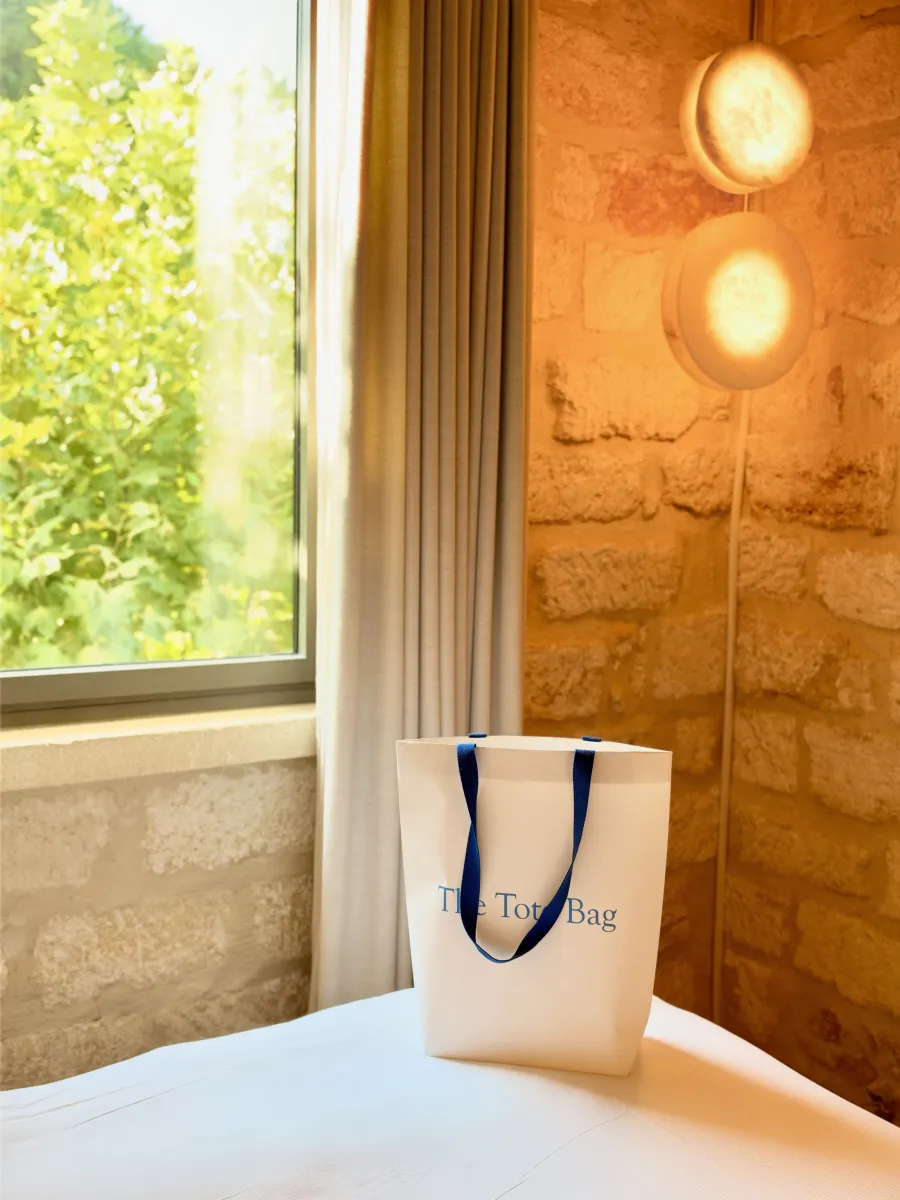 The Tote Bag debout sur un lit, sous deux appliques en pierre.